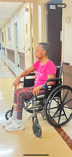 An elderly person in a wheelchair, sitting quietly in a hospital corridor.
