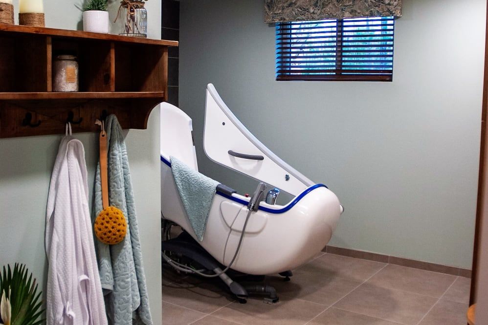 A modern bathroom featuring a sleek, white bathtub with towels hanging nearby and a window with blinds.