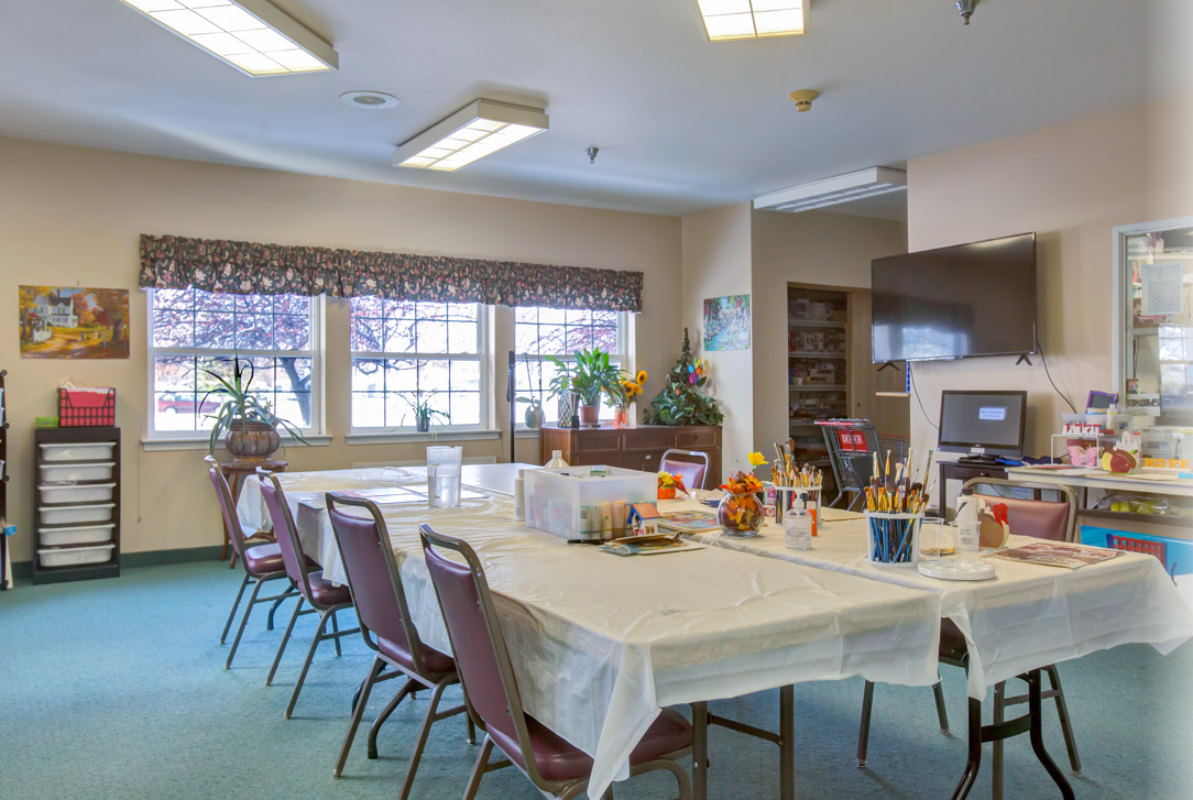 A well-lit dining or meeting room with tables and chairs arranged, featuring large windows and various decorations.