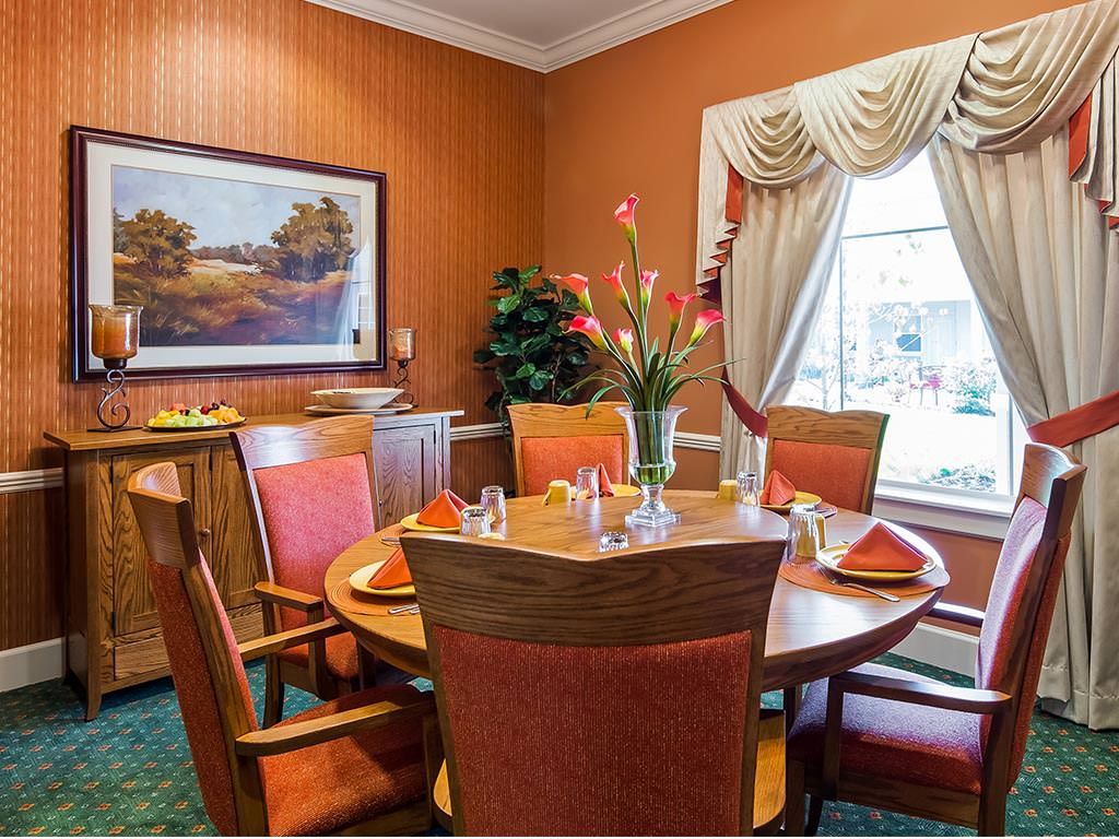 A cozy dining room with a round table set for four, decorated with a vase of flowers and surrounded by red cushioned chairs.