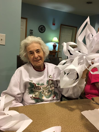 An elderly woman proudly showcasing her paper snowflake craft during a creative session.