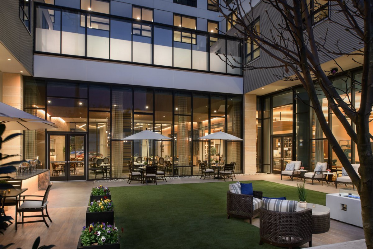 A modern hotel courtyard with outdoor seating and large windows, set in an evening ambiance.