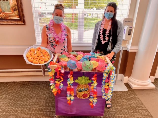 Two people in masks stand by a colorful, Hawaiian-themed cart with snacks.