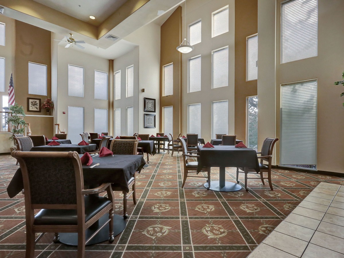 A spacious dining room with high ceilings, large windows, and neatly arranged tables and chairs.