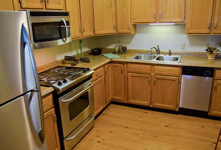 A modern kitchen with wooden cabinets and flooring, featuring a stove, microwave, and sink.