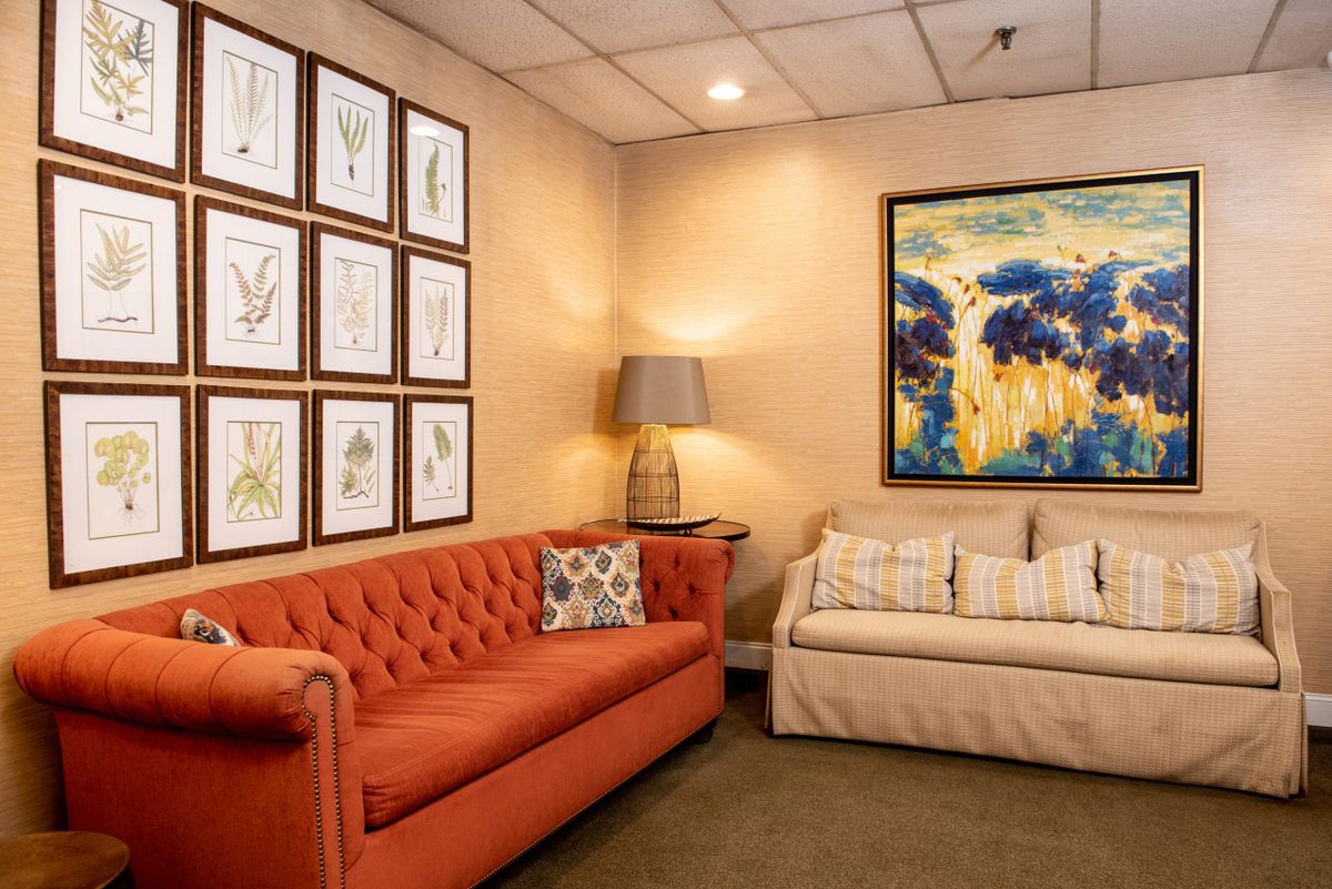 A cozy living room featuring a red sofa, a beige couch, and various artworks on the walls.