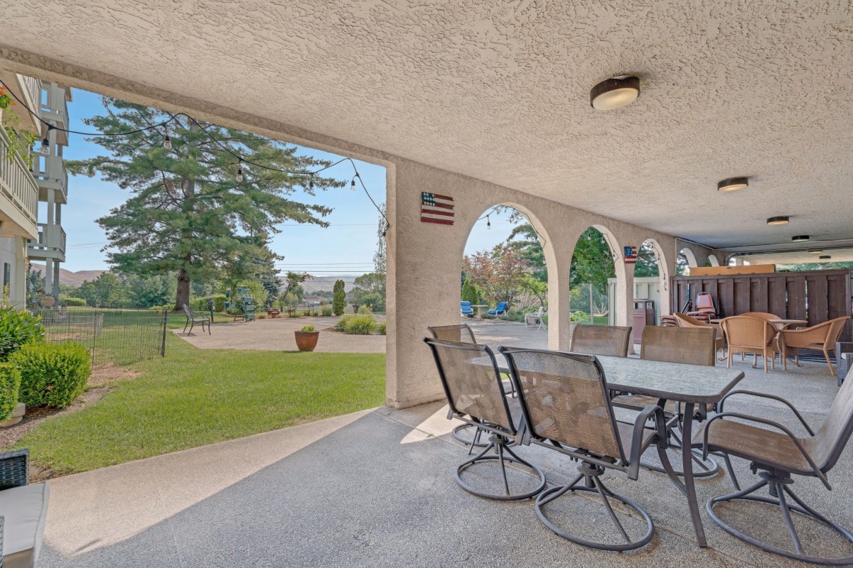 A spacious patio with outdoor furniture overlooking a garden and yard, featuring arched openings for an open view.