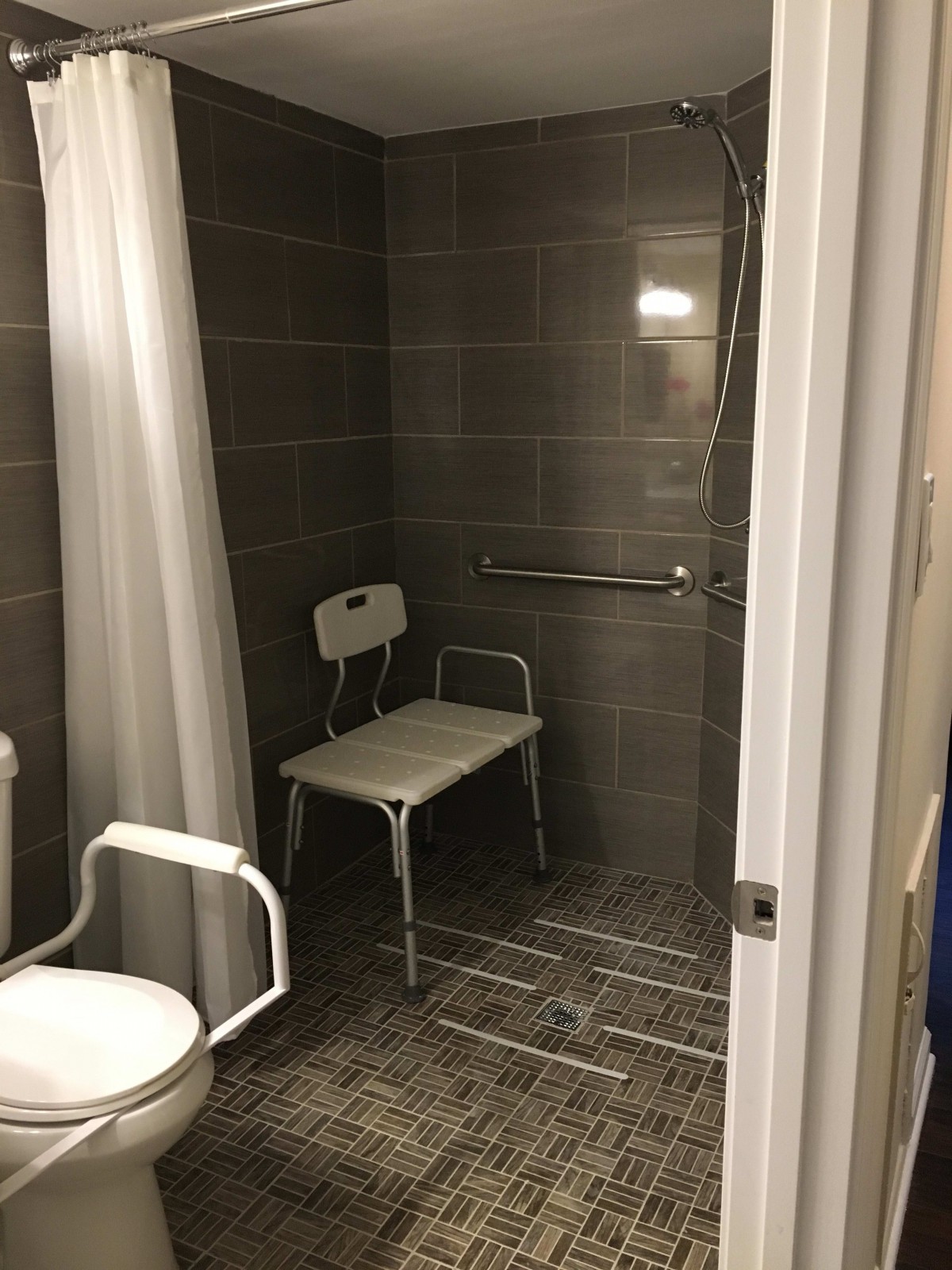 An accessible bathroom featuring a shower area with a chair and grab bar.