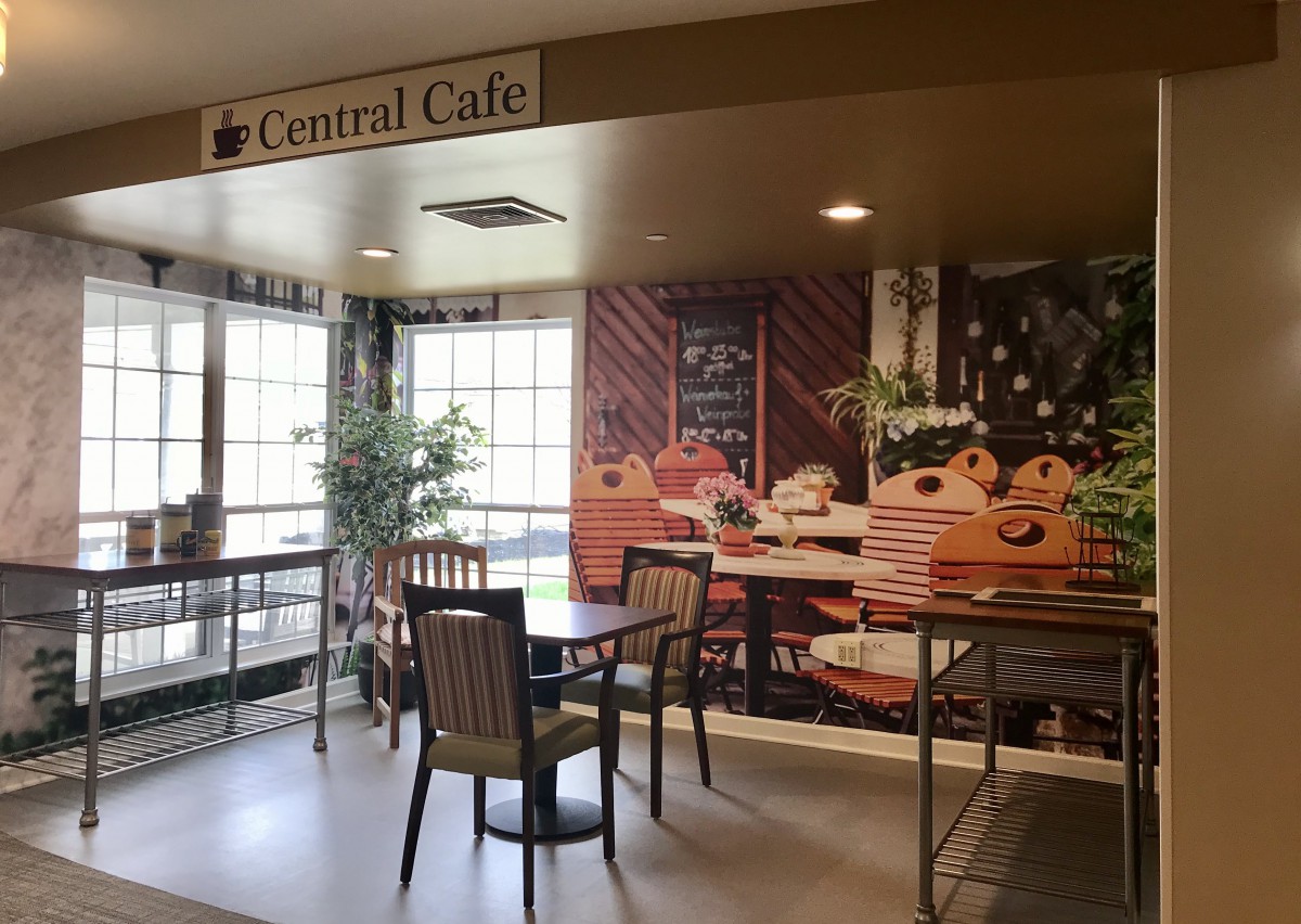 A cozy cafe interior with tables and chairs, adorned with plants and warm decor.