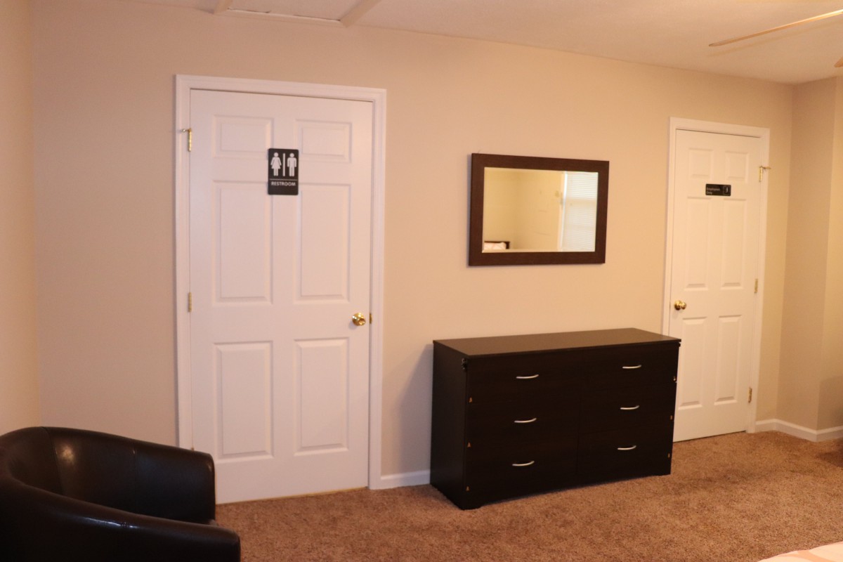 A neatly arranged bedroom featuring a dresser with a mirror above it and two doors.