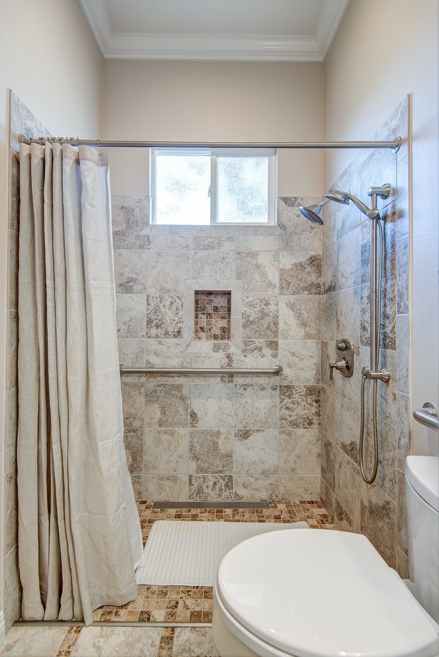 A modern bathroom featuring a tiled shower area with a curtain and a small window.