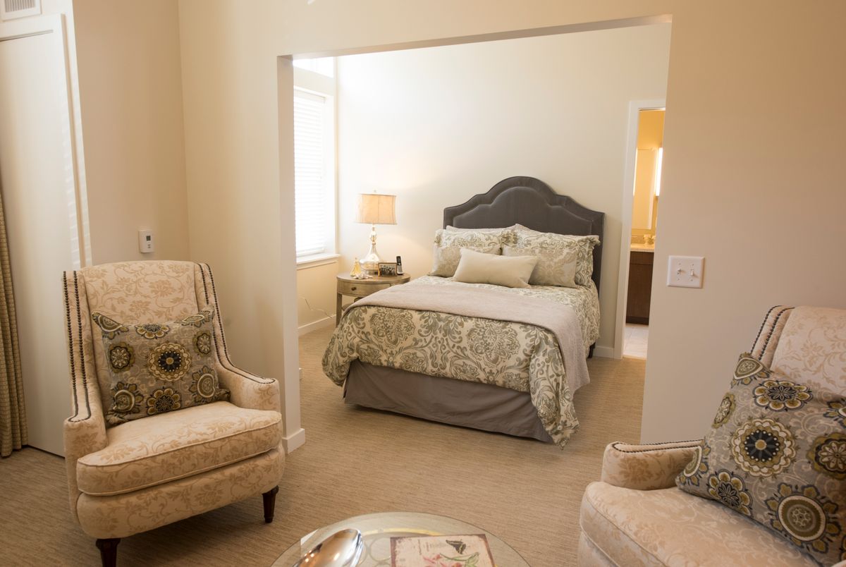 A cozy bedroom with a neatly made bed, armchairs, and warm lighting.