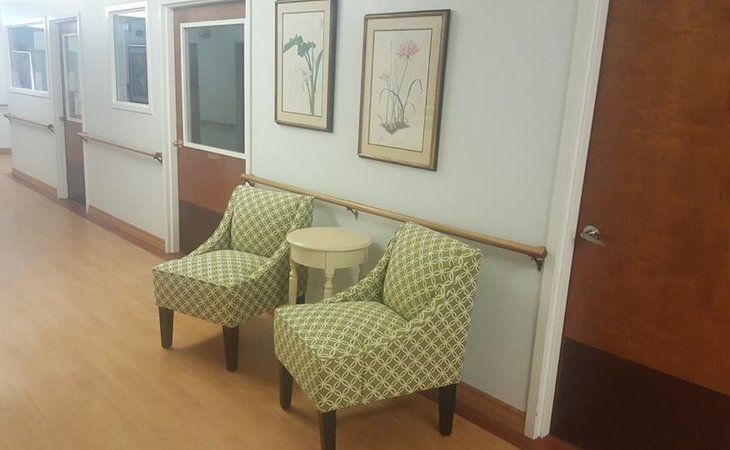 A seating area in a hallway with two patterned chairs, a small table, and framed floral artwork on the wall.