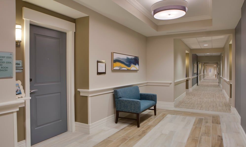 A well-lit hallway with an armchair and a painting on the wall.