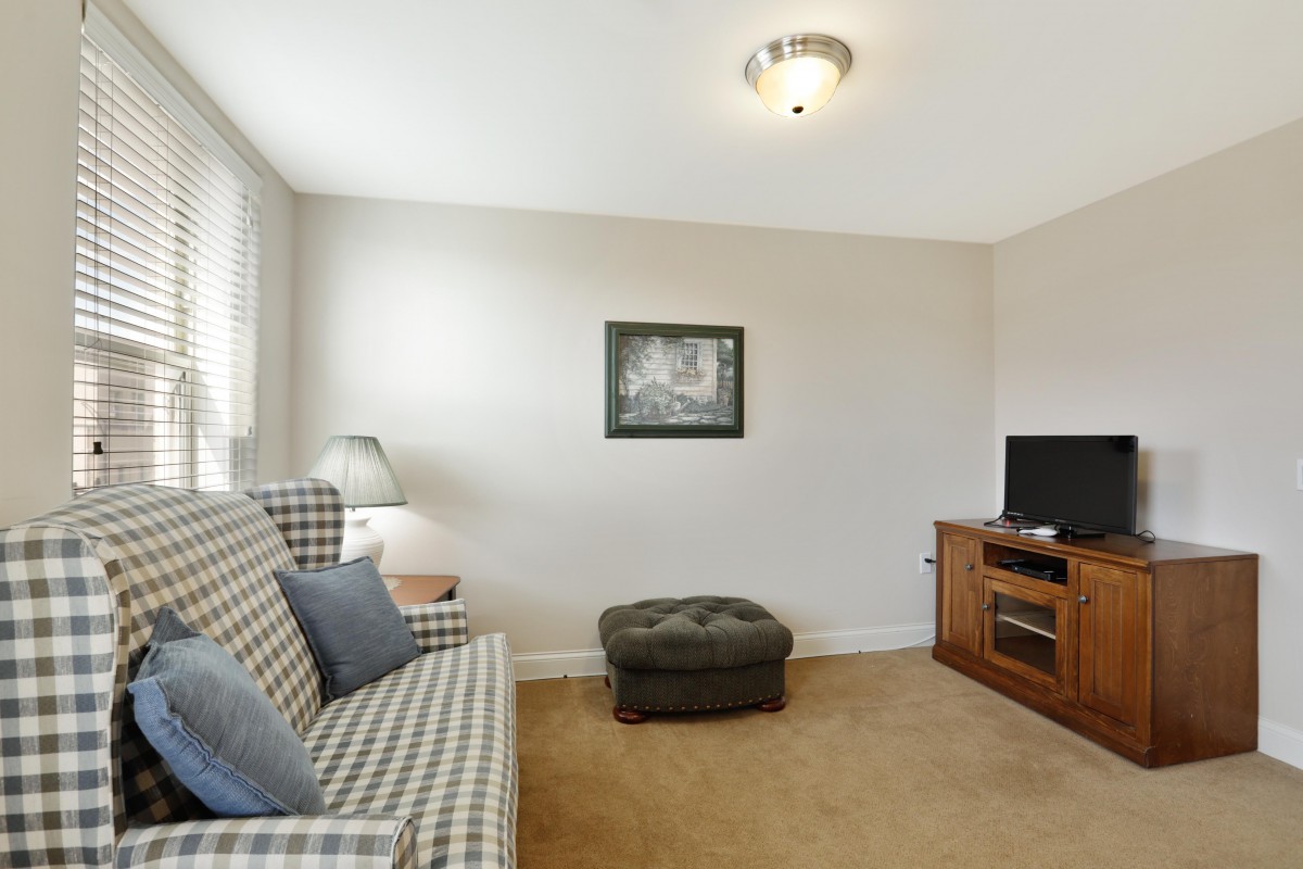 A cozy living room with a patterned sofa, ottoman, and a television on a wooden stand.
