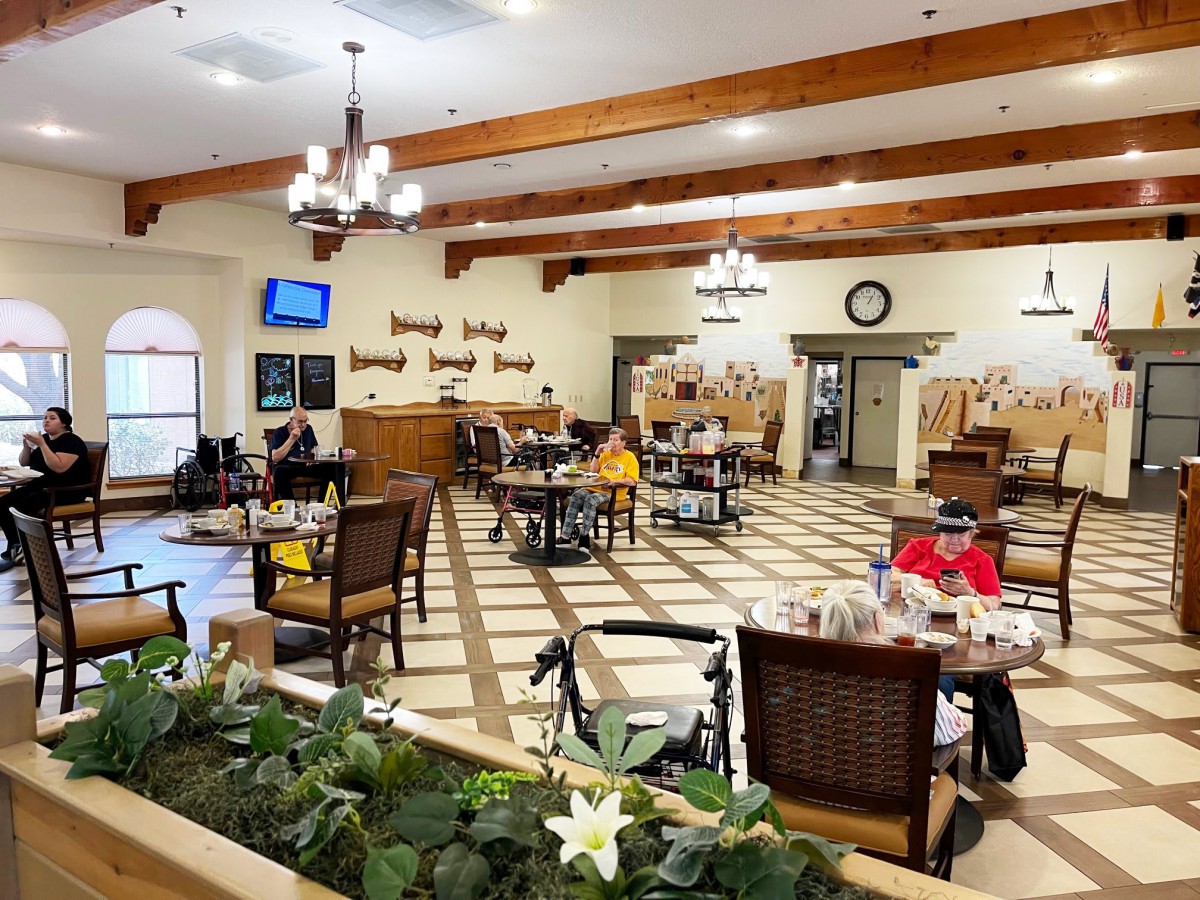 A spacious dining area with wooden beams, chandeliers, and several people seated at tables.