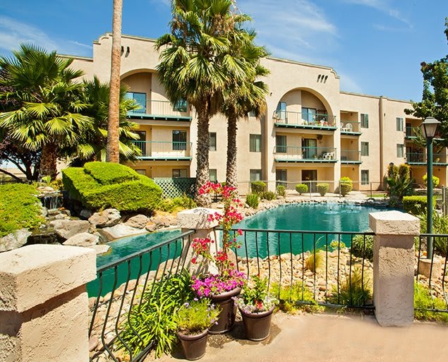 A sunny day at a residential apartment complex with a pool and lush landscaping.