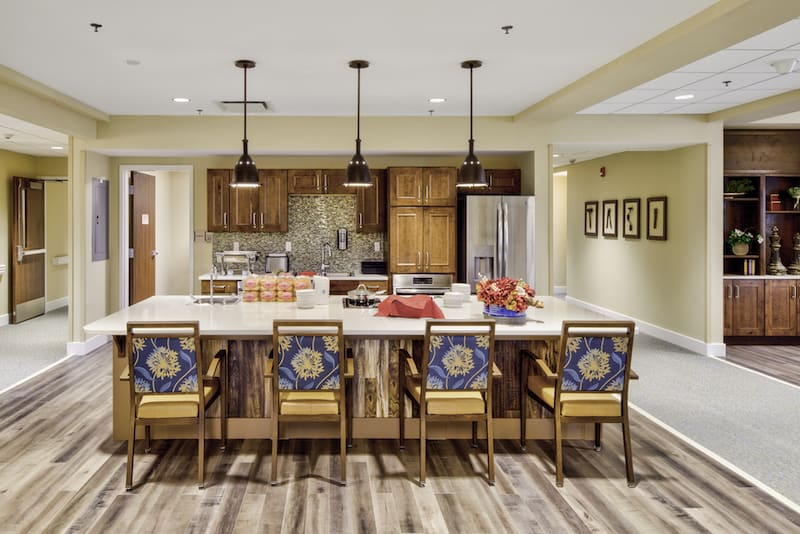 A modern kitchen with a large island and colorful seating, featuring pendant lighting and wooden cabinets.
