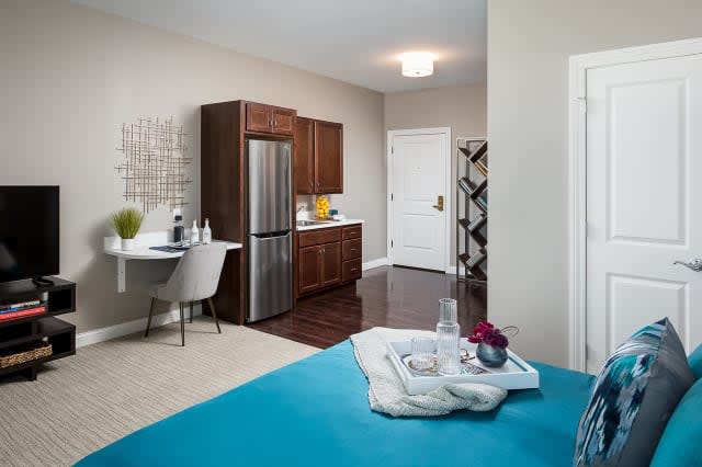 A modern apartment interior featuring a minimalist kitchen with stainless steel appliances and wooden cabinets, alongside a compact workspace.