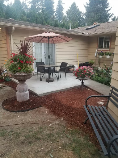 A cozy patio area featuring a table and chairs under an umbrella, surrounded by vibrant flowers and well-maintained landscaping.