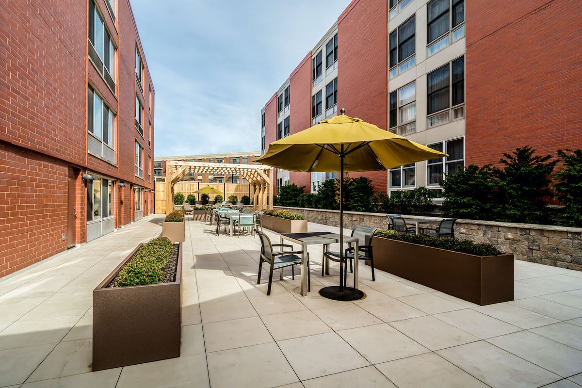 A modern outdoor patio area with tables, chairs, and umbrellas set between two buildings.