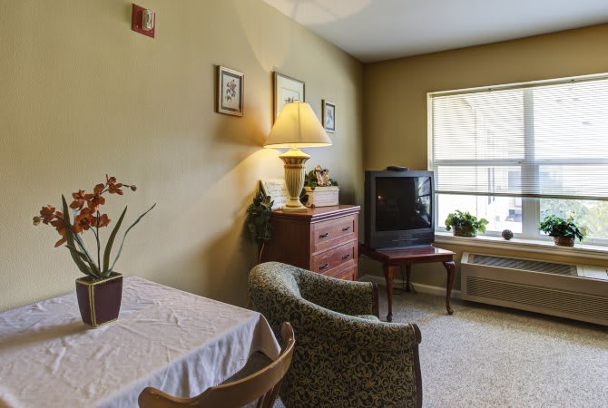A cozy living room with a television, upholstered chairs, and a small table with decor.