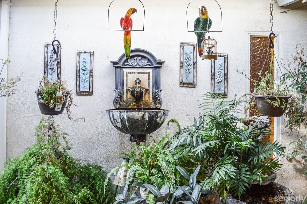 An indoor space adorned with lush plants, decorative parrots, and a central fountain feature surrounded by wall art.