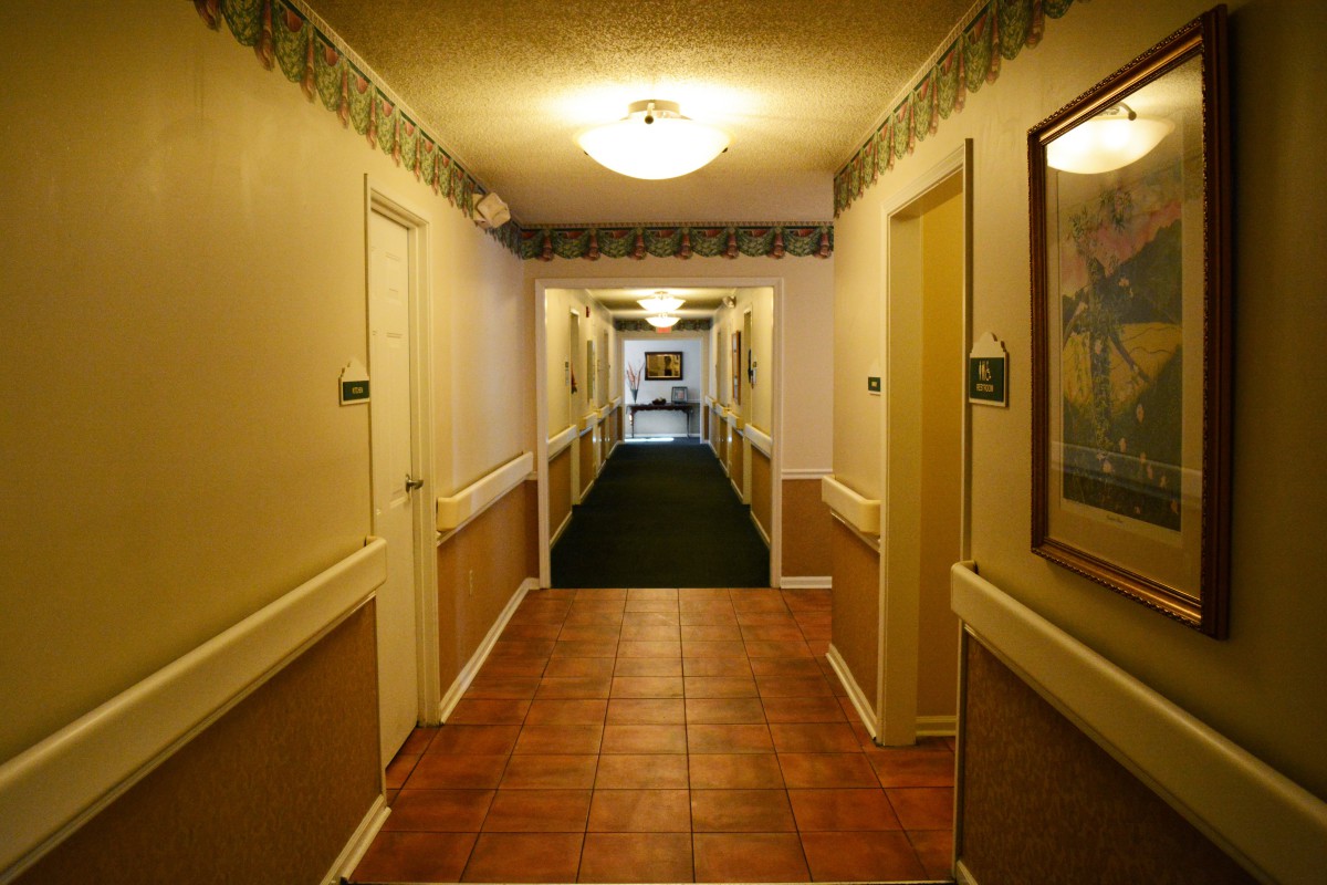 A well-lit hotel hallway with doors and framed artwork along the walls.