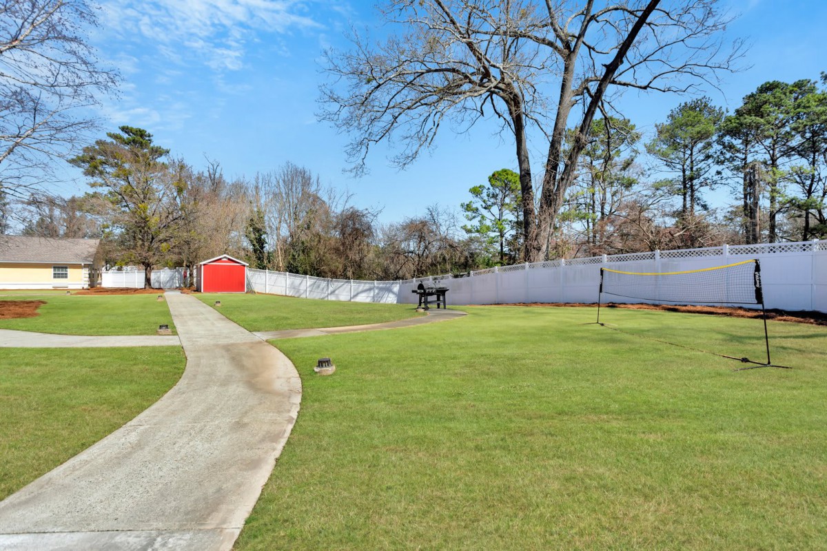 A well-maintained backyard with a green lawn, a pathway leading to a red shed, and surrounded by a white fence.