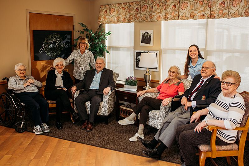A group of seniors and caregivers seated together in a cozy indoor setting.