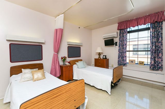 A clean and comfortable hospital room with two beds, curtains, and windows.