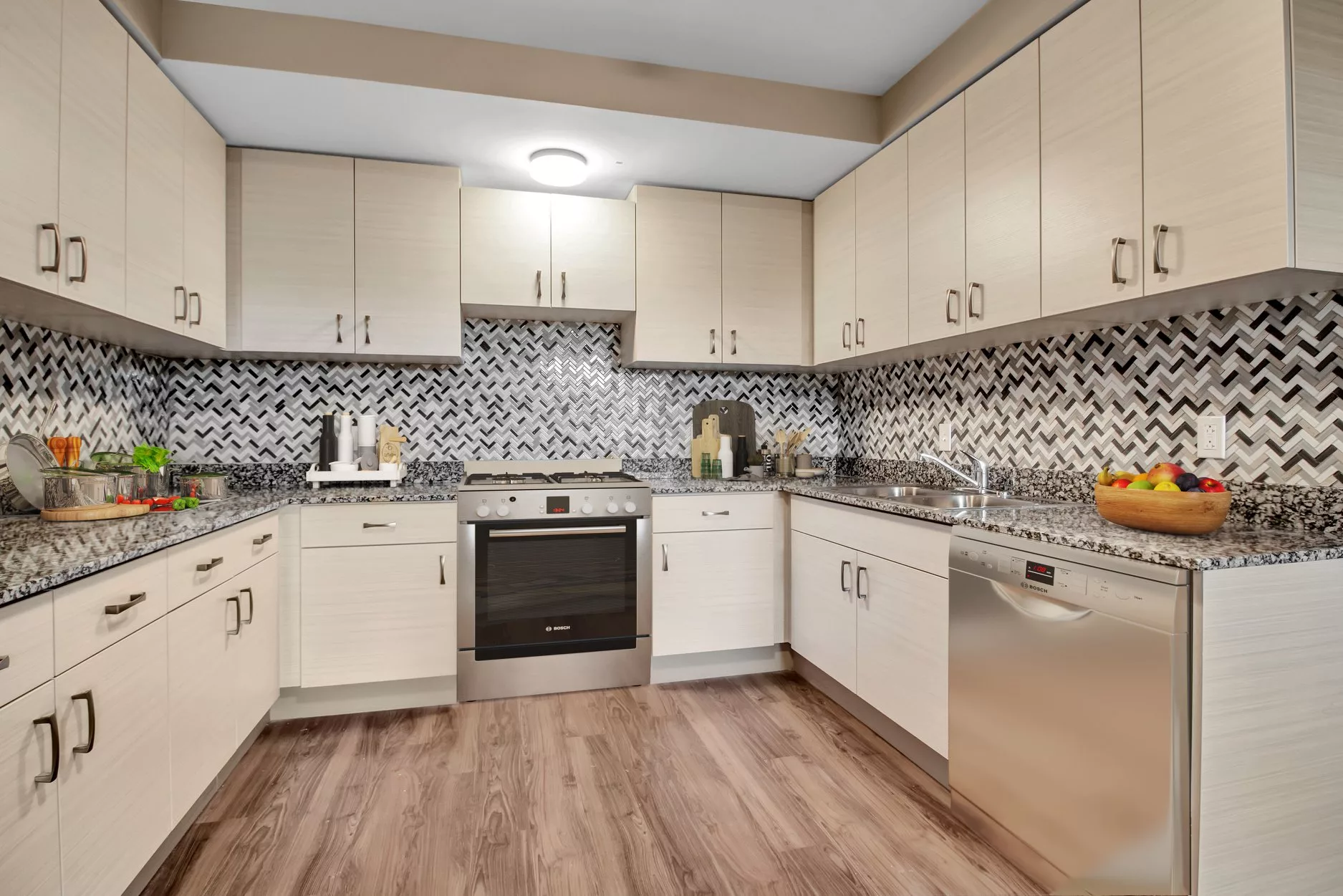 A modern kitchen featuring white cabinets, a patterned backsplash, and hardwood flooring.