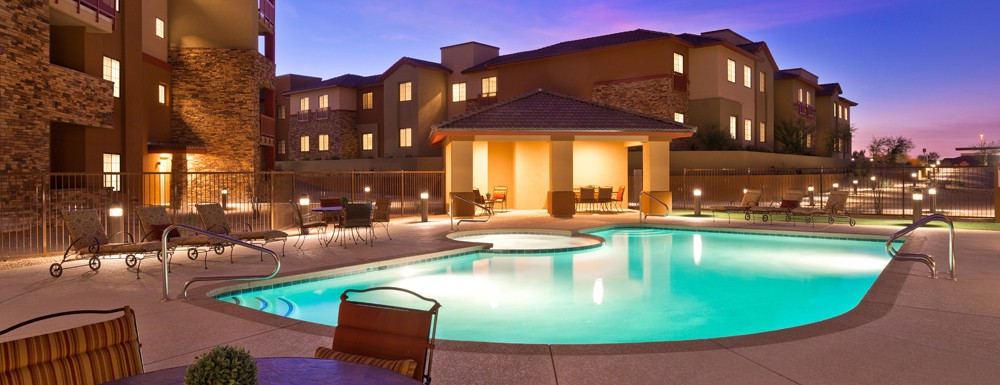 A well-lit outdoor pool area at a resort during the evening.