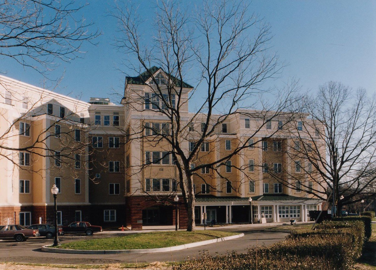A mid-rise residential building with bare trees in front, under a clear blue sky.