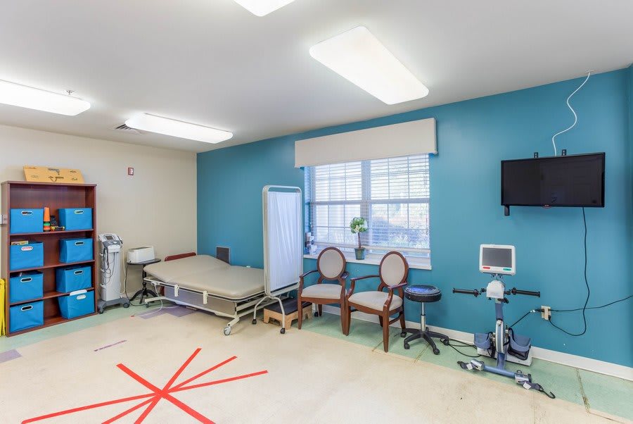 A rehabilitation room with exercise equipment and seating in a medical facility.
