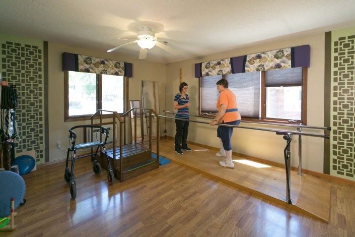 A rehabilitation therapy room with exercise equipment and two individuals engaging in physical therapy activities.