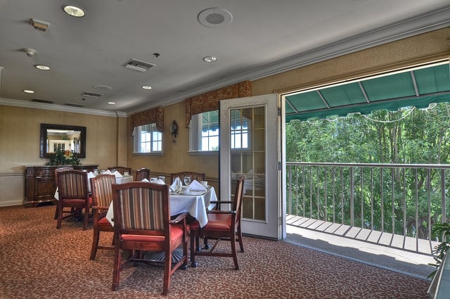 A cozy dining room with elegantly set tables, offering a scenic balcony view.