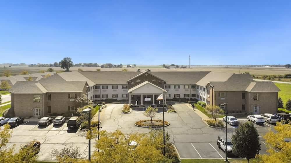 A residential building with a parking lot and landscaped surroundings under a clear blue sky.
