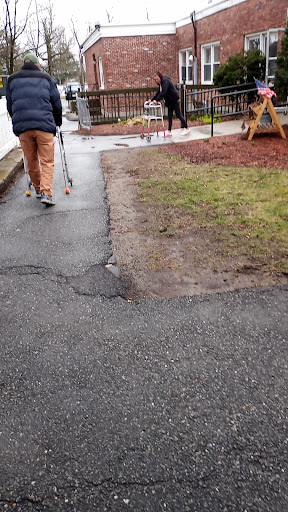 An elderly person using a walker on a pathway near a playground.