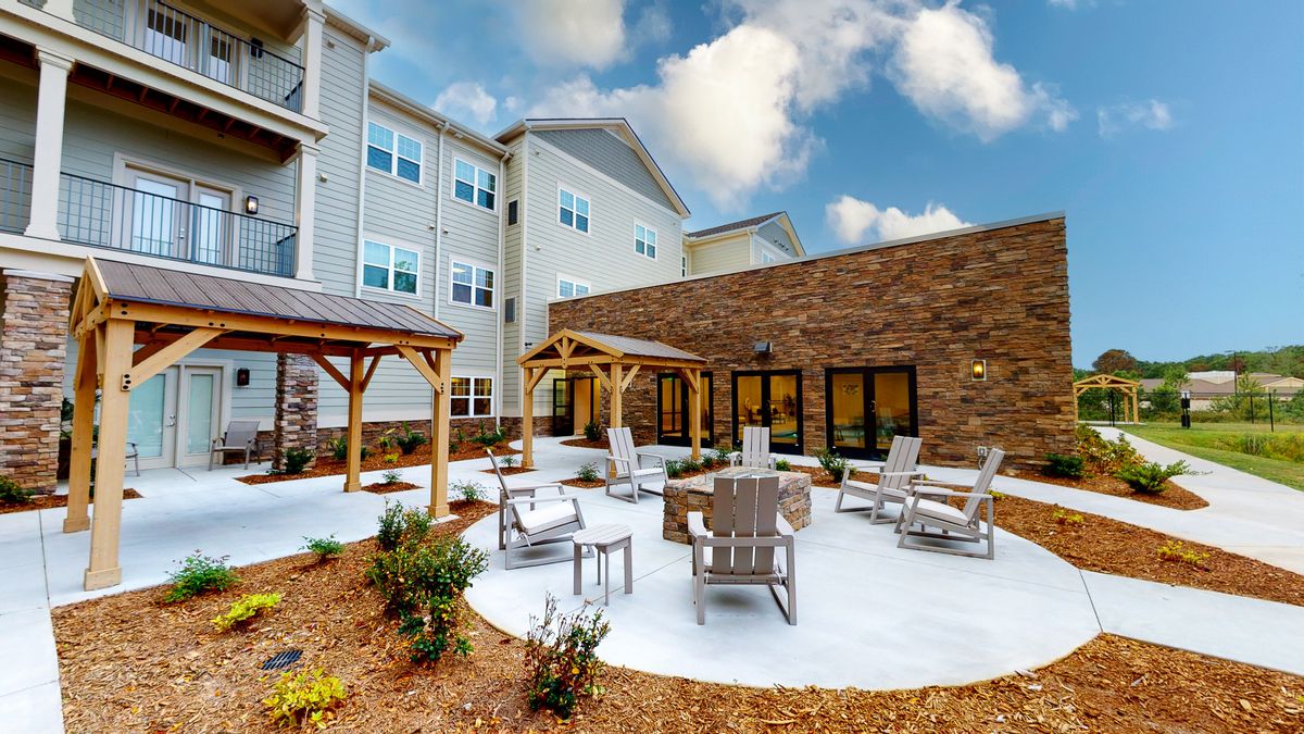An inviting outdoor patio area with seating and pergolas in front of an apartment building.