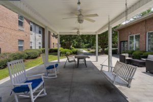 A covered patio with rocking chairs and a table at an apartment complex.
