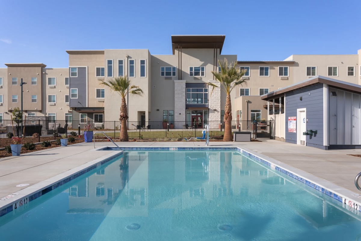 A modern apartment complex with a large outdoor pool and palm trees in the foreground.