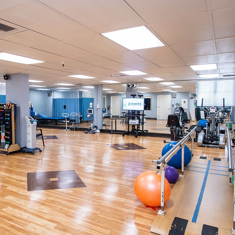 A spacious gym with various fitness equipment, wooden floors, and large mirrors.