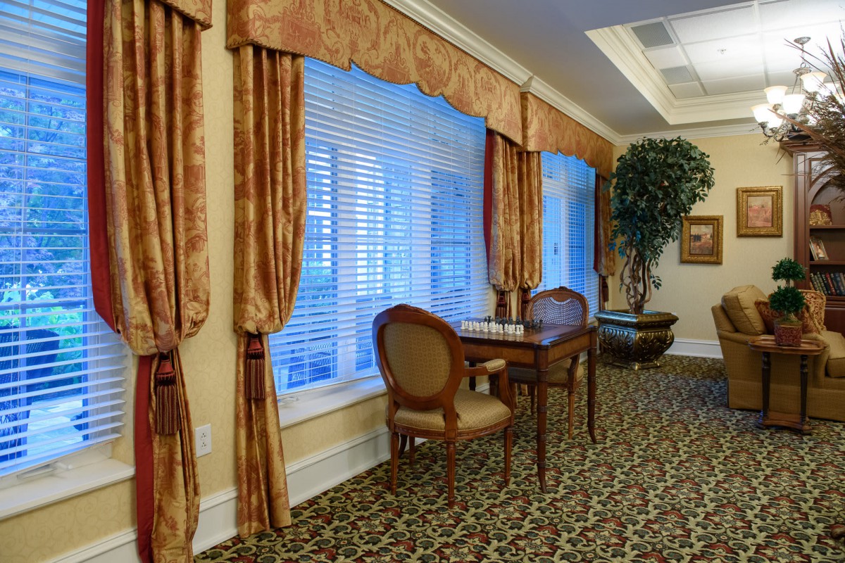 A warmly decorated room with elegant curtains, a patterned carpet, and a small table with chairs by the window.