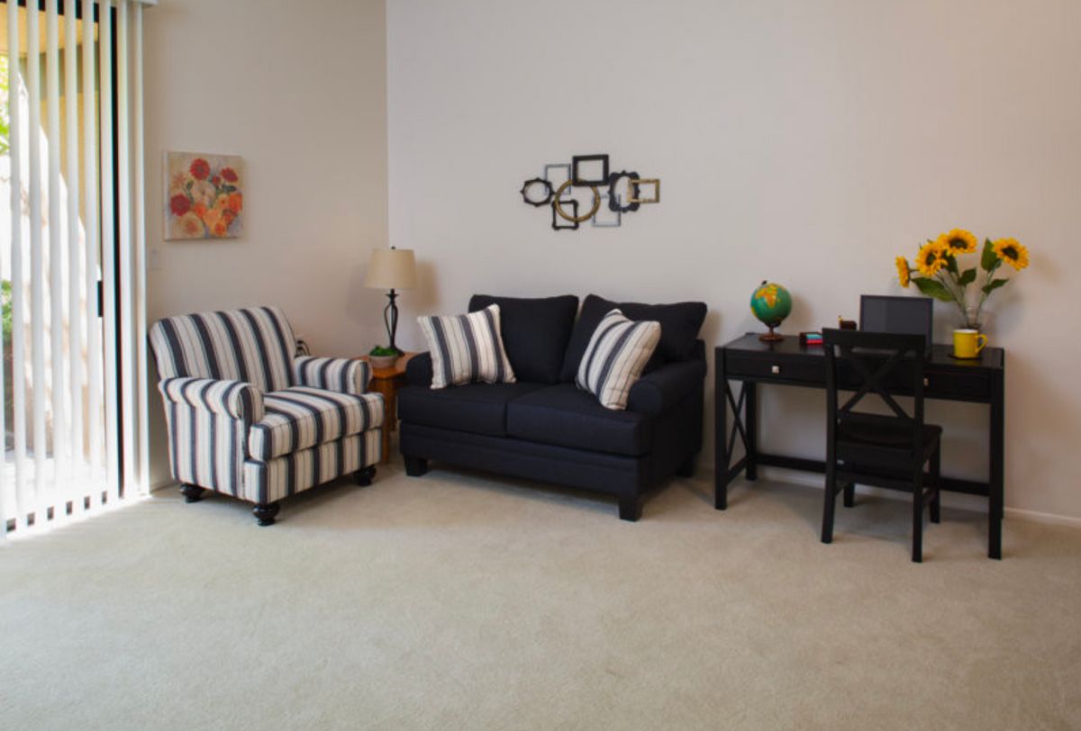A cozy living room with a striped armchair and a dark sofa, complemented by a desk and decorative wall art.