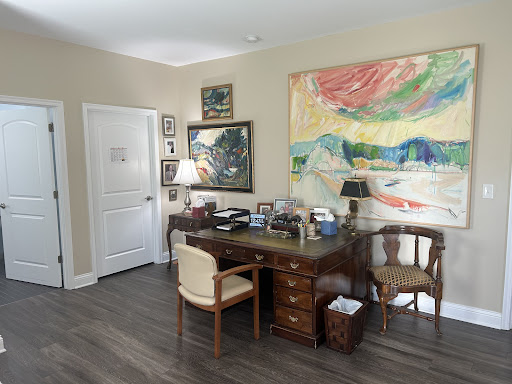 A cozy office space featuring a wooden desk, comfortable chairs, and colorful artwork on the wall.