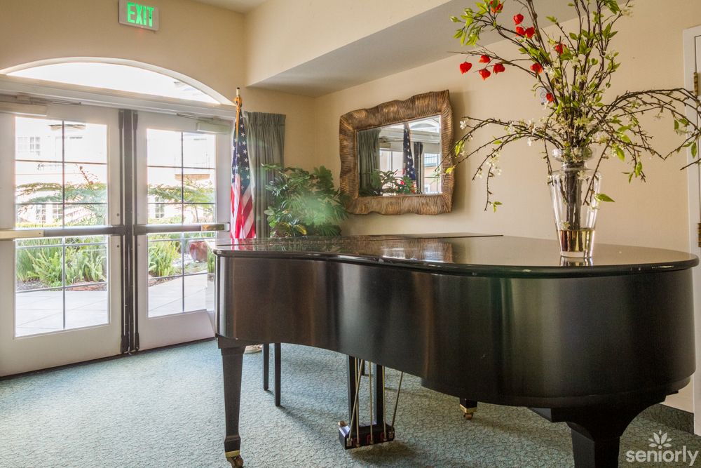 A grand piano in a well-lit room with decorative flowers, a mirror, and an American flag.