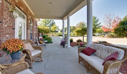 A spacious porch with wicker furniture and pillows overlooks a landscaped garden.