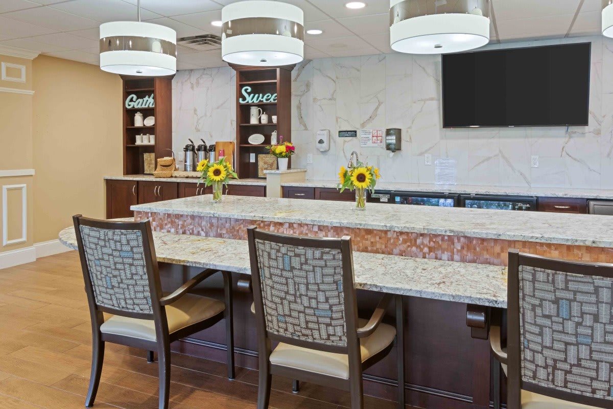 A modern kitchen area with a decorative counter, chairs, and sunflowers.