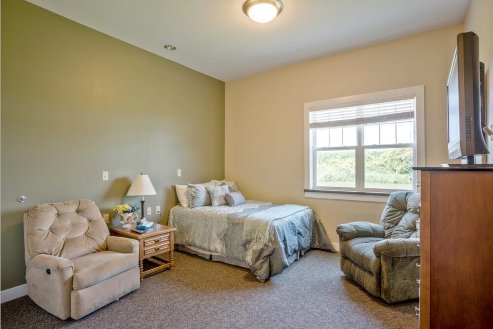 A cozy bedroom with a bed, two chairs, and a window providing natural light.